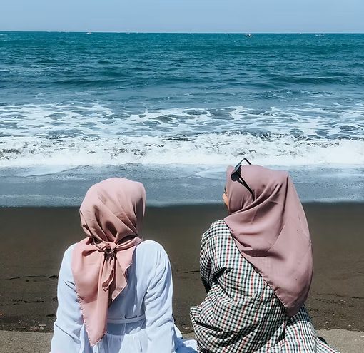 Two women in hijab sitting by the sea